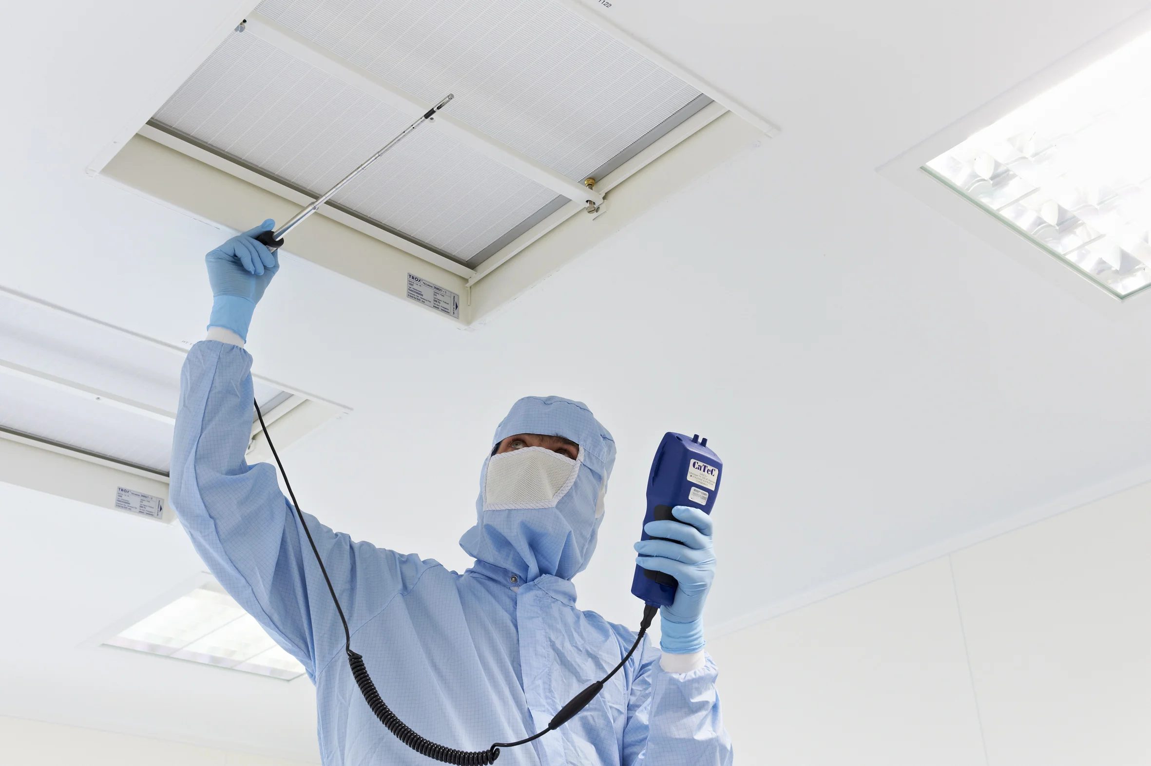 Technician with particle counter and probe at HEPA ceiling filter in cleanroom – EU GMP Annex 1 air monitoring